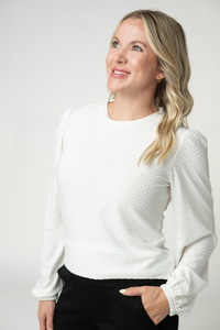 Woman wearing a white textured sweater against a plain background