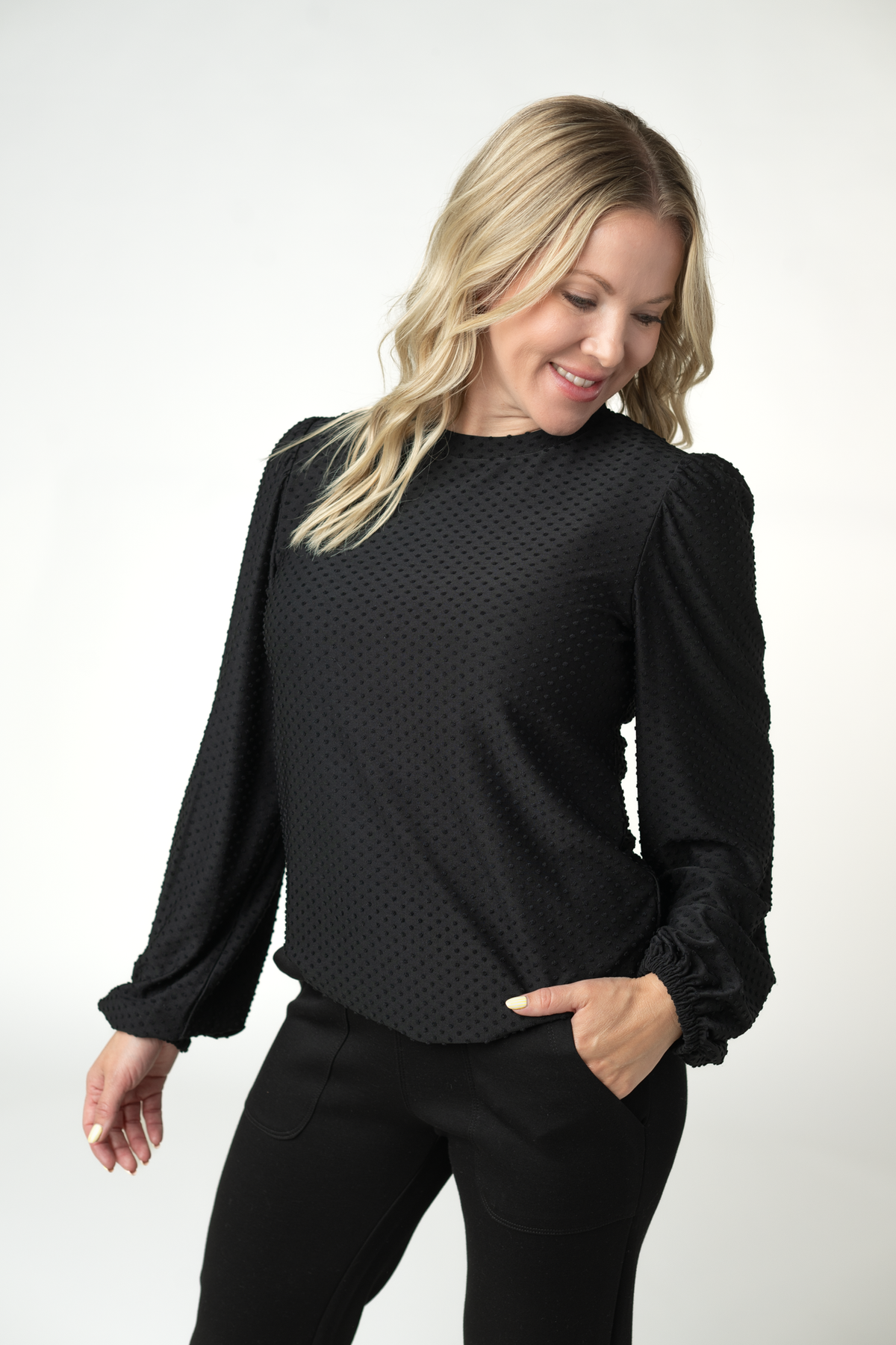 Woman wearing a black textured blouse with long sleeves on a white background