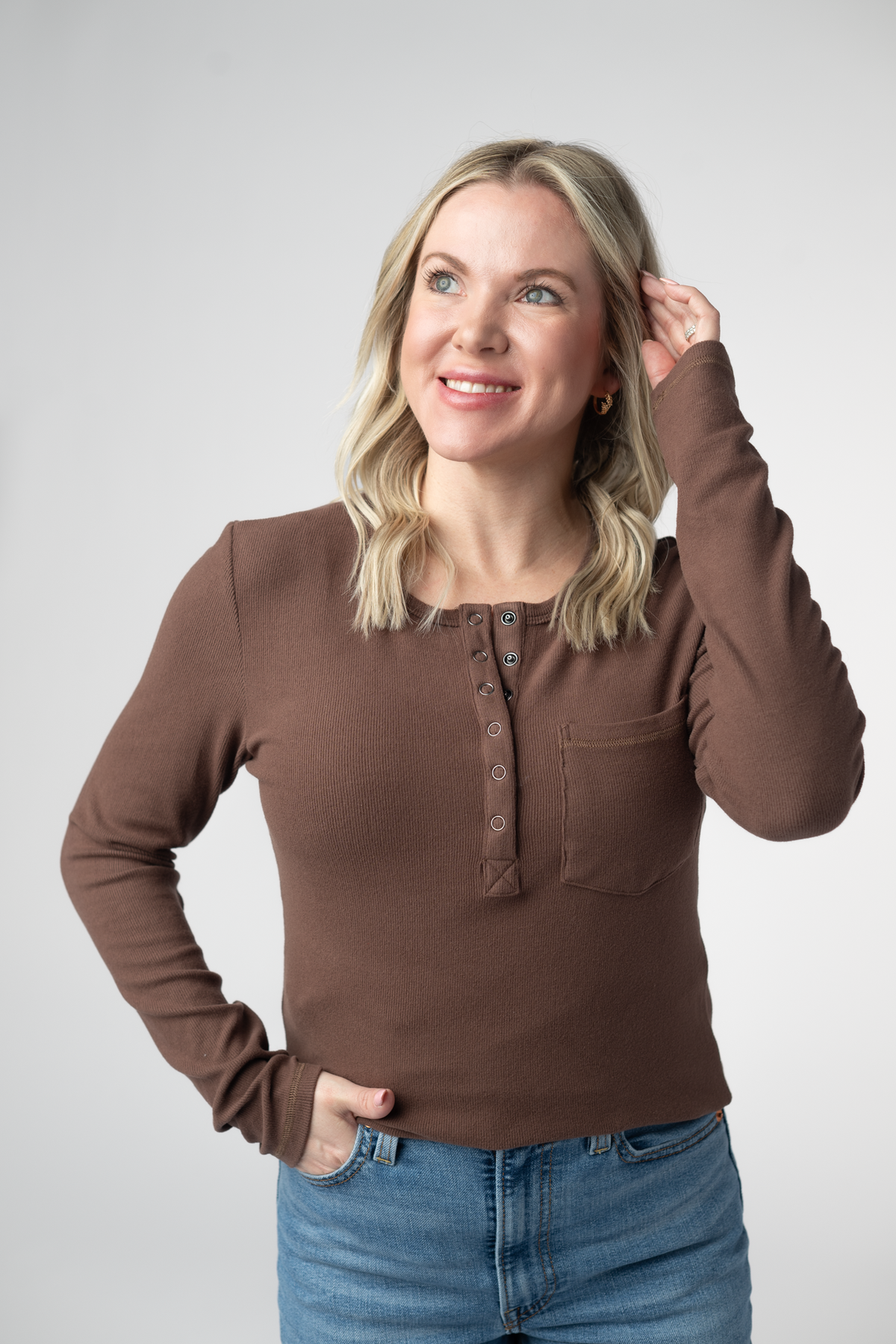 Woman wearing a brown long-sleeve shirt and blue jeans against a white background
