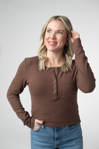 Woman wearing a brown long-sleeve shirt and blue jeans against a white background