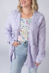 Woman wearing a light purple cardigan over a floral top and jeans on a plain background