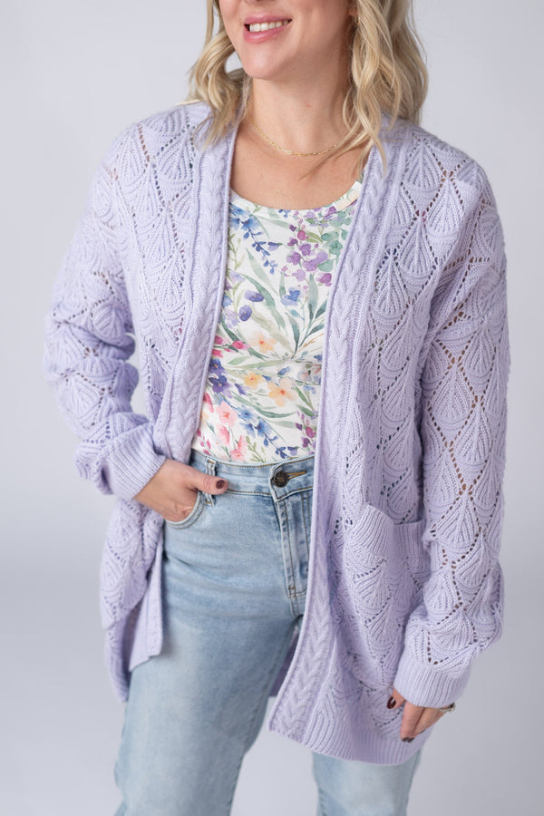 Woman wearing a light purple cardigan over a floral top and jeans on a plain background