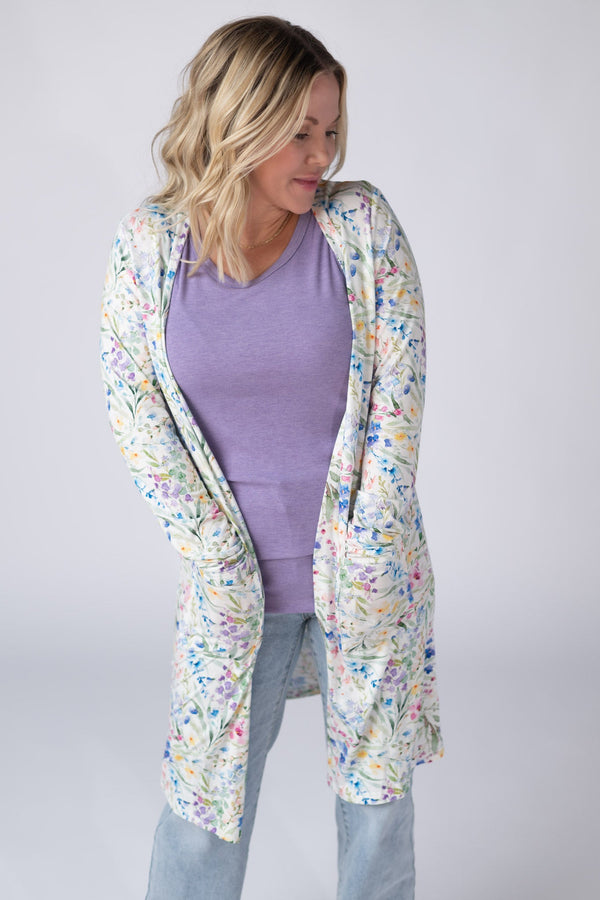 Woman wearing a floral cardigan over a purple top and light blue jeans on a plain background