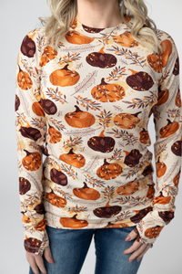 Person wearing a long-sleeve shirt with pumpkins and leaves pattern on a plain background