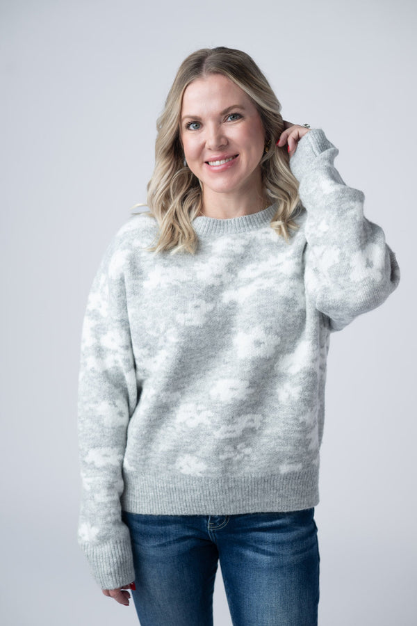 Woman wearing a light gray sweater with a subtle pattern on a plain background