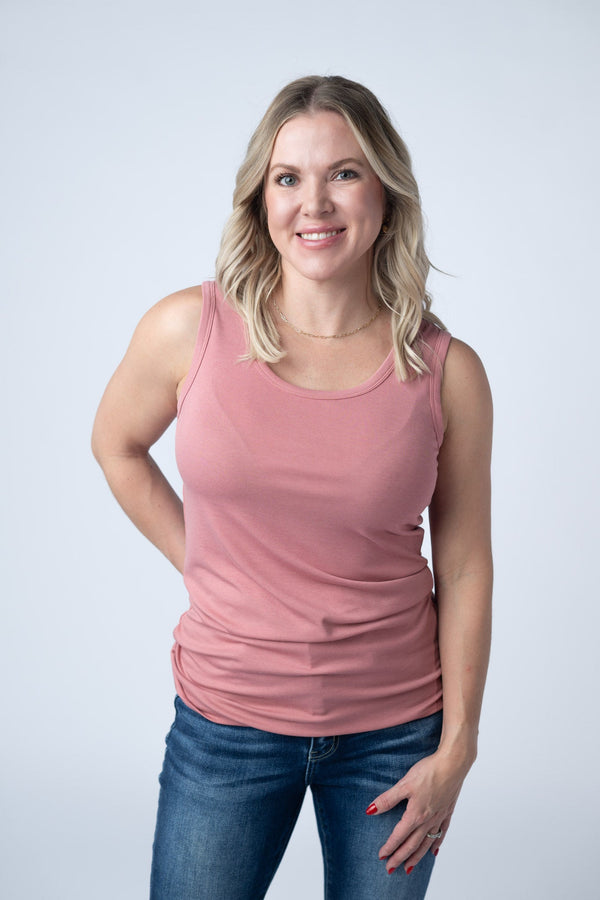 Woman wearing a pink tank top and blue jeans against a white background