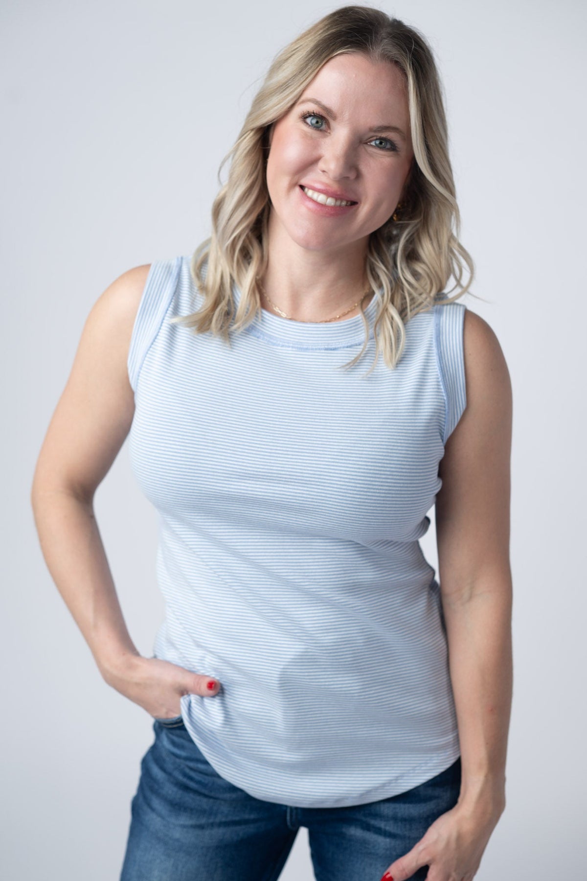 Woman wearing a light blue sleeveless top and jeans against a plain background