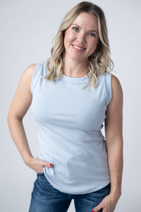 Woman wearing a light blue sleeveless top and jeans against a plain background