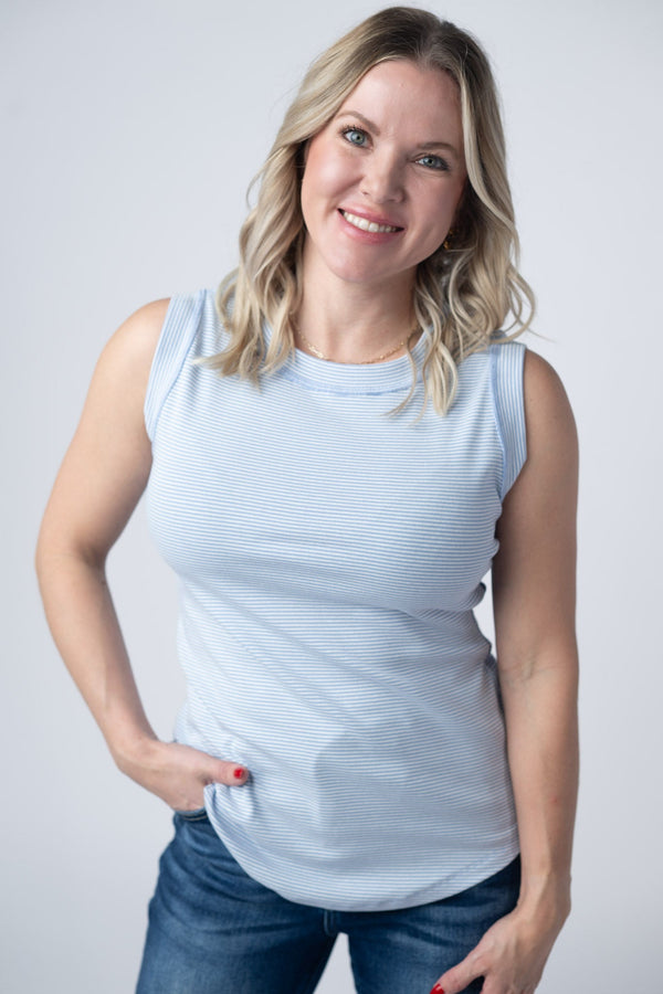 Woman wearing a light blue sleeveless top and jeans against a plain background