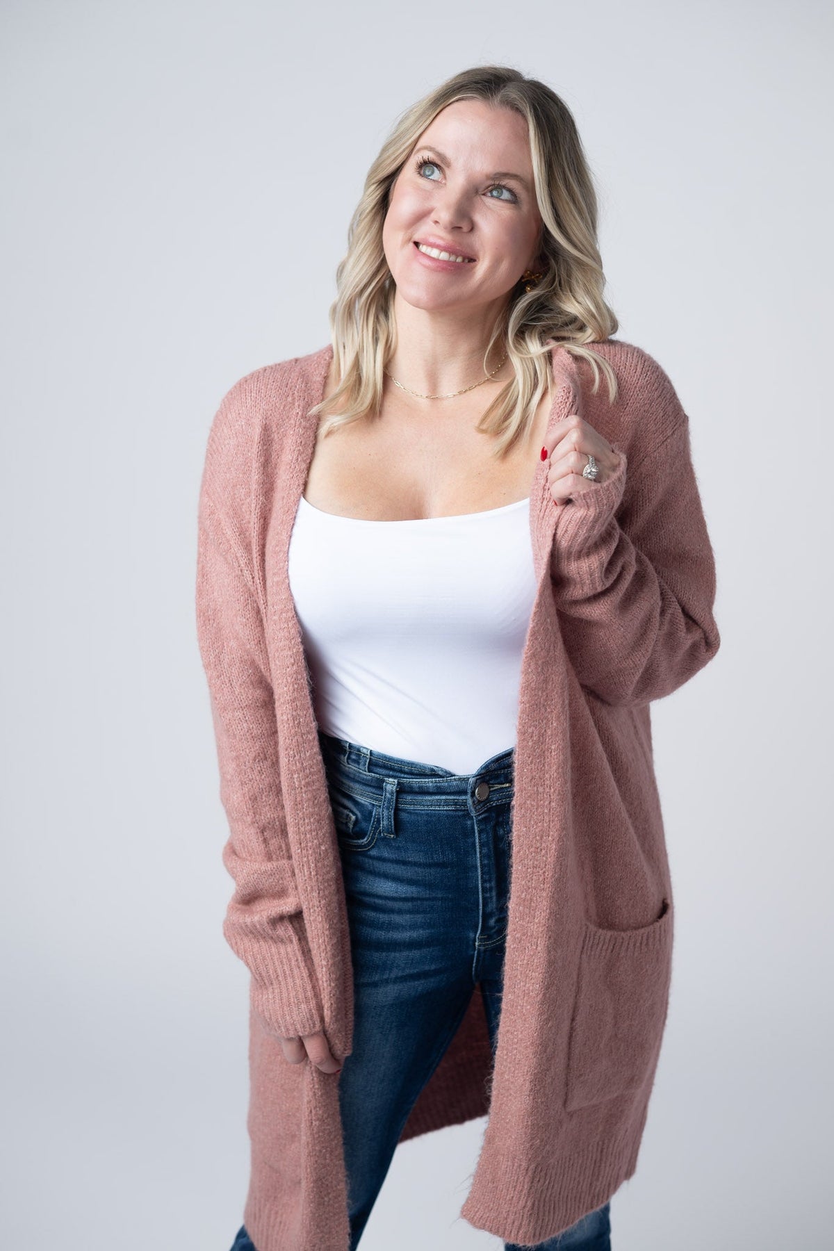 Woman wearing a pink cardigan over a white top and blue jeans on a plain background