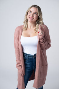 Woman wearing a pink cardigan over a white top and blue jeans on a plain background