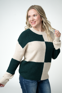 Woman wearing a color-blocked sweater with green, beige, and navy sections on a white background.