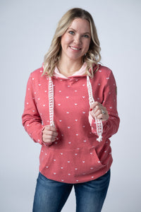 Woman wearing a pink hoodie with heart patterns on a plain background