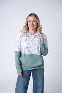 Woman wearing a green and white floral hoodie with blue jeans on a white background