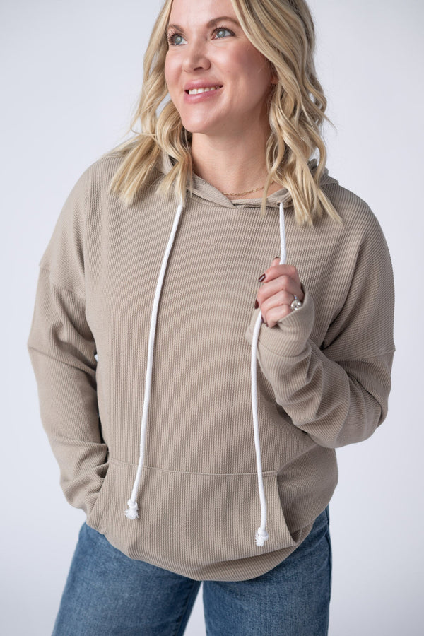Woman wearing a beige hoodie with white drawstrings on a plain background