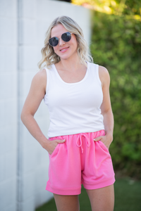 Woman wearing a white tank top and pink shorts outdoors.