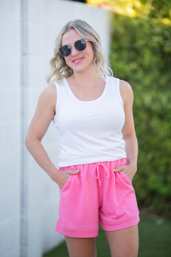 Woman wearing a white tank top and pink shorts outdoors.