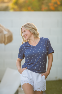 Woman wearing a blue patterned shirt and white shorts outdoors.