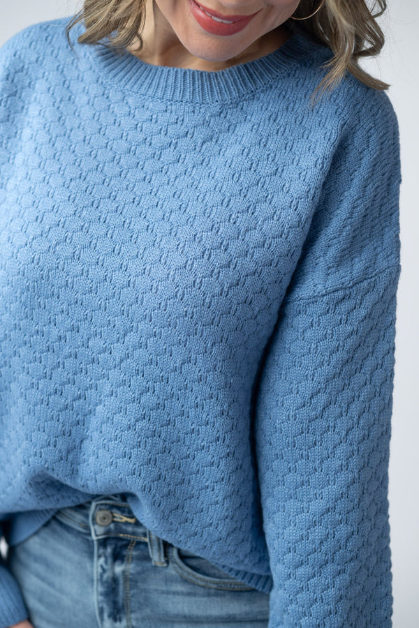 Person wearing a blue knitted sweater against a white background