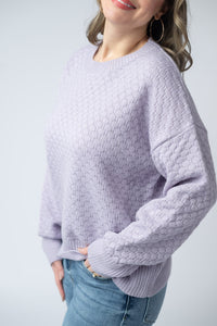 Person wearing a textured light purple sweater against a plain background