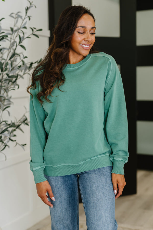Woman wearing a teal sweatshirt and blue jeans standing indoors.