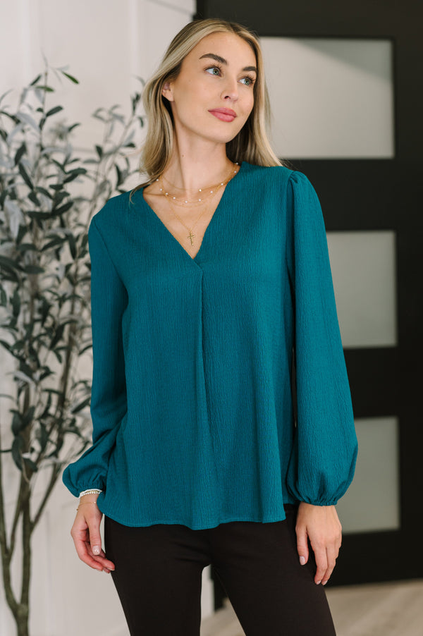 Woman wearing a teal blouse with long sleeves in an indoor setting