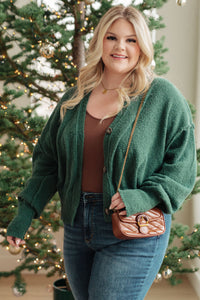 Woman wearing a green cardigan and holding a brown handbag in front of a decorated Christmas tree.