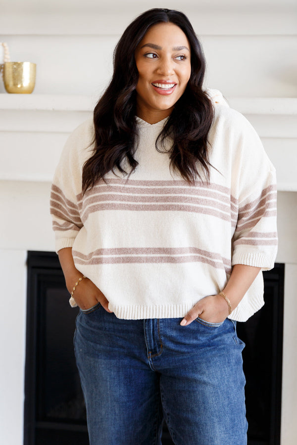 Woman wearing a striped sweater and blue jeans standing in a room with a fireplace.