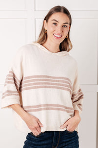 Woman wearing a cream sweater with brown stripes against a white background
