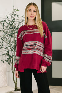 Woman wearing a red sweater with patterned sleeves standing indoors.