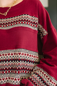 Close-up of a red sweater with patterned sleeves and hem.