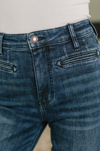Close-up of a person wearing dark blue denim jeans with a white top visible at the waist.