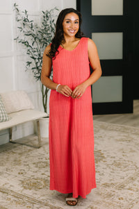 Woman wearing a coral dress standing in a room with a plant and furniture.