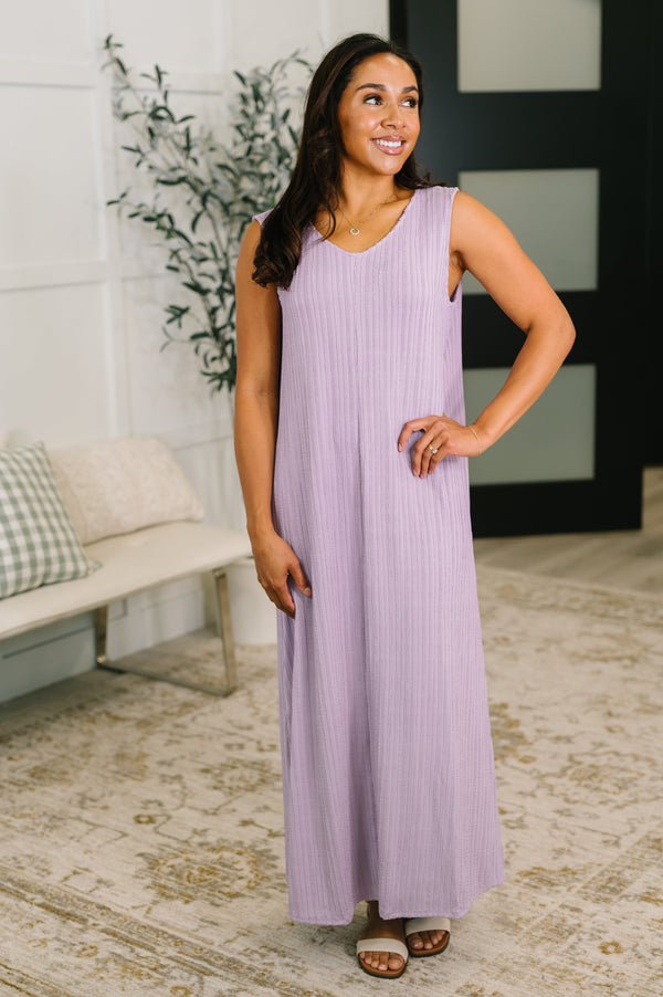 Woman wearing a purple dress standing in a room with a plant and sofa.