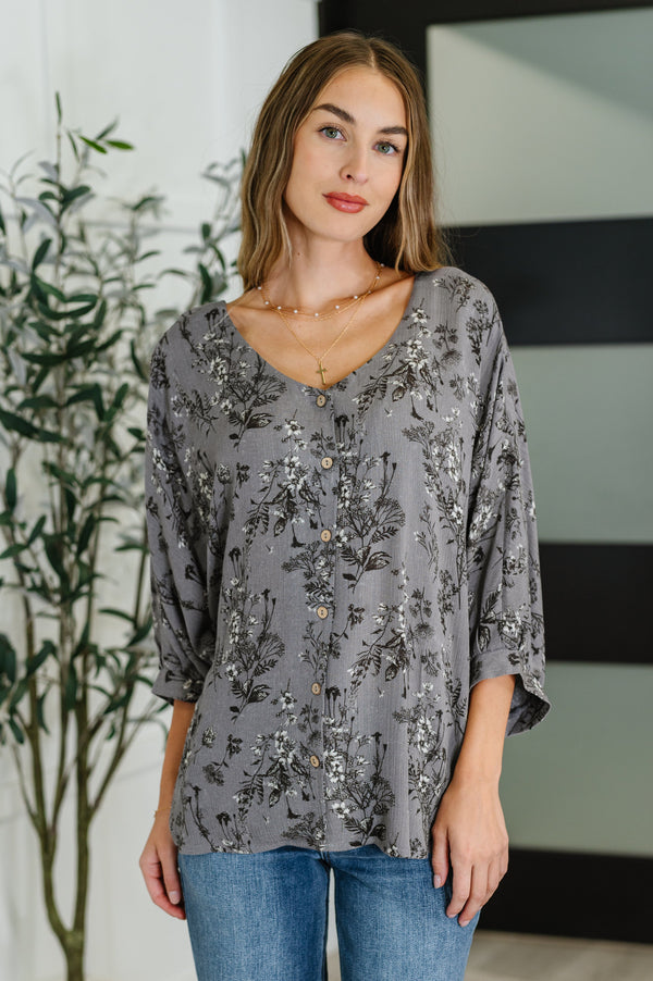 Woman wearing a gray floral blouse with blue jeans indoors.