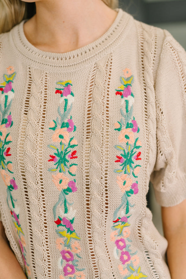 Beige knit sweater with colorful floral embroidery on a blurred background