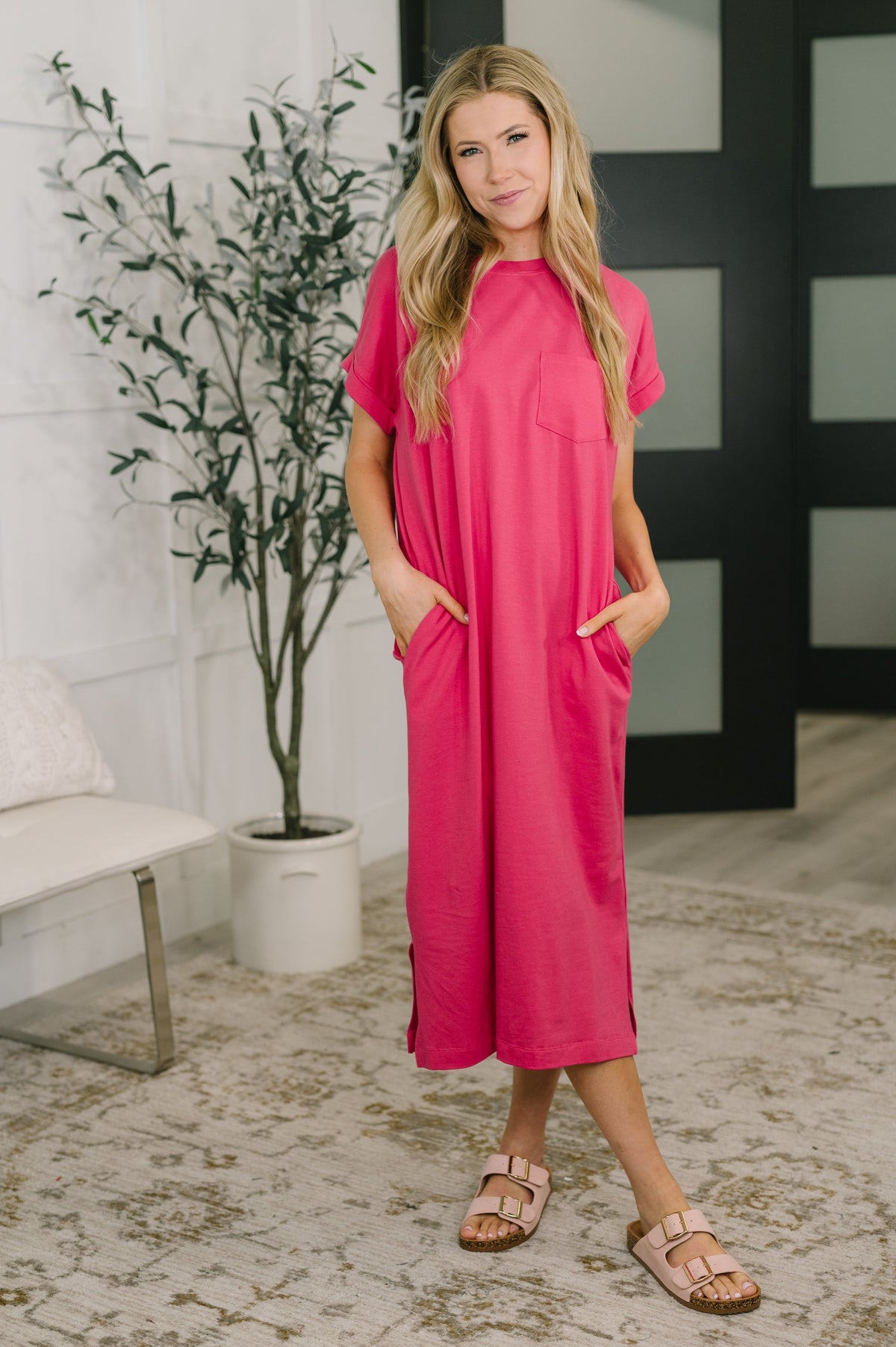 Woman wearing a bright pink dress standing in a room with a plant and a black and white abstract painting.