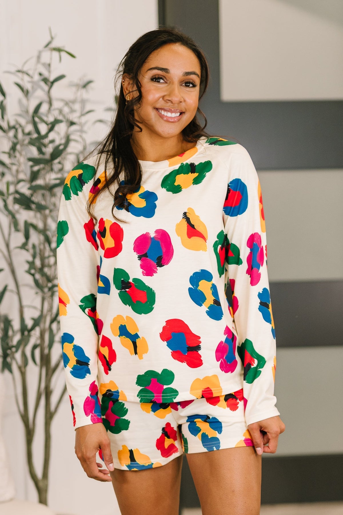 Woman wearing a colorful floral outfit in a room with a plant and white couch.
