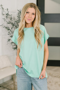 Woman wearing a light green top and blue jeans indoors.