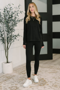 Woman wearing a black outfit with white sneakers standing indoors.