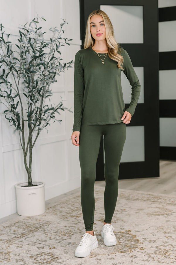 Woman wearing a green outfit standing indoors with a plant and decorative wall in the background