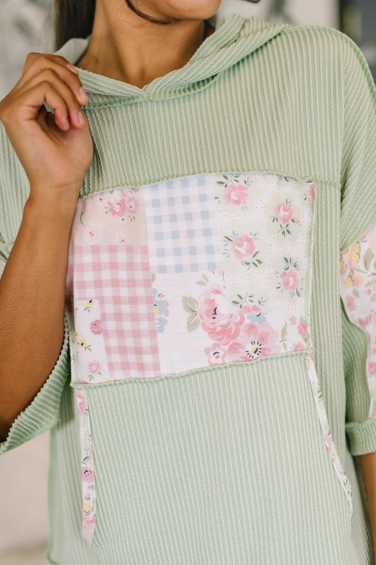 Green ribbed sweater with a floral and checkered patch pocket.