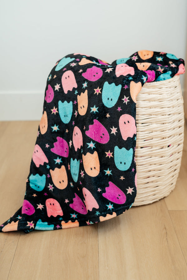 Colorful ghost patterned blanket draped over a wicker basket on a wooden floor.