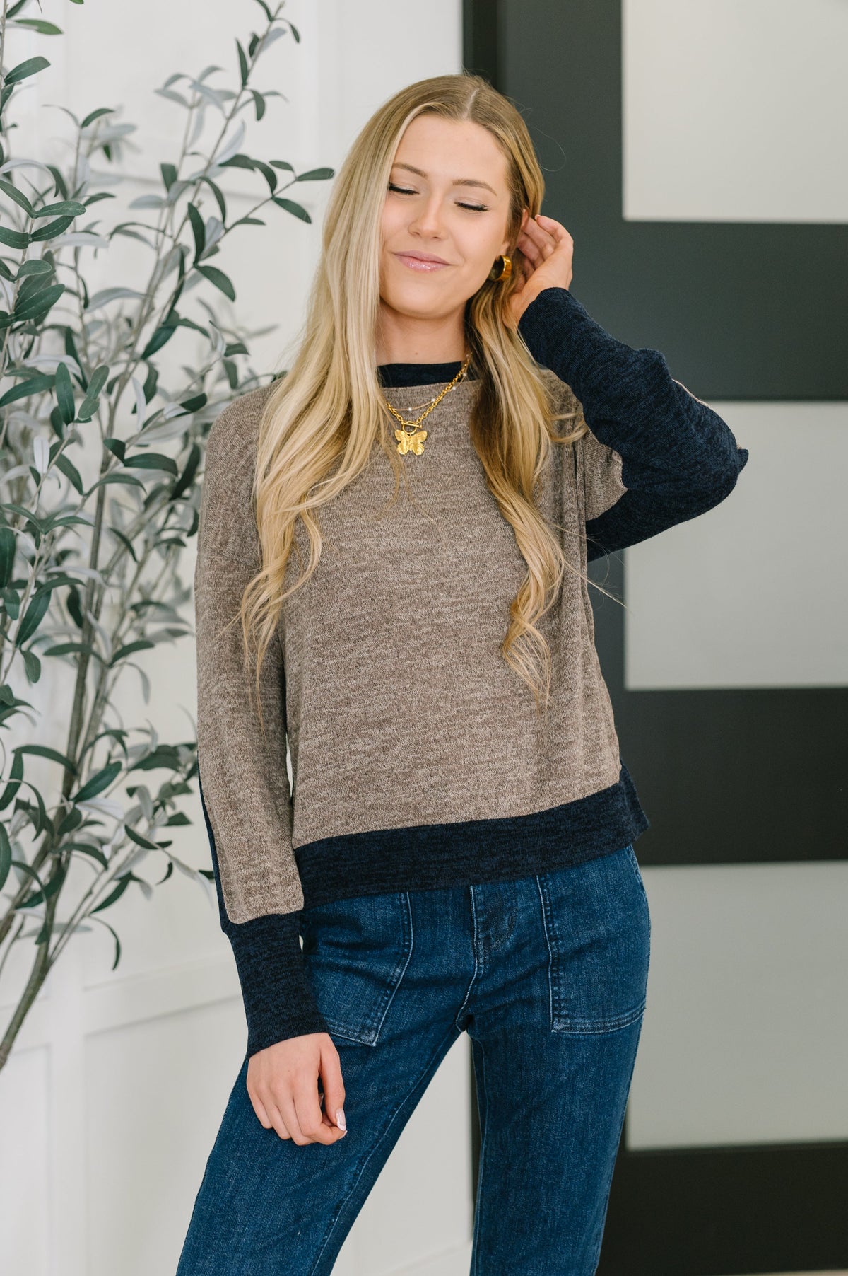 Woman wearing a brown sweater and blue jeans with a plant in the background