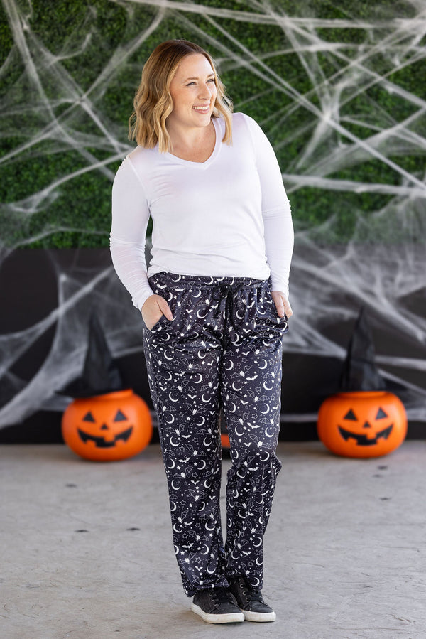 Woman wearing a white long-sleeve top and navy moon-patterned pants in front of Halloween decorations.