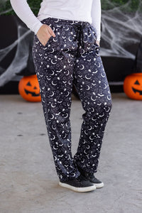 Person wearing dark pants with moon and star pattern in front of Halloween decorations.