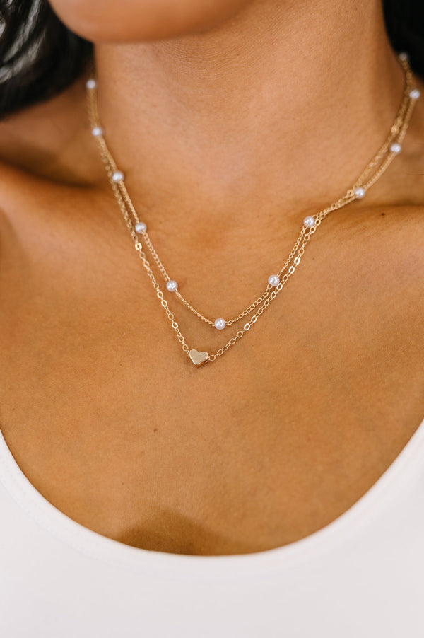 Close-up of a person wearing a delicate gold necklace with small heart pendants on a plain background.