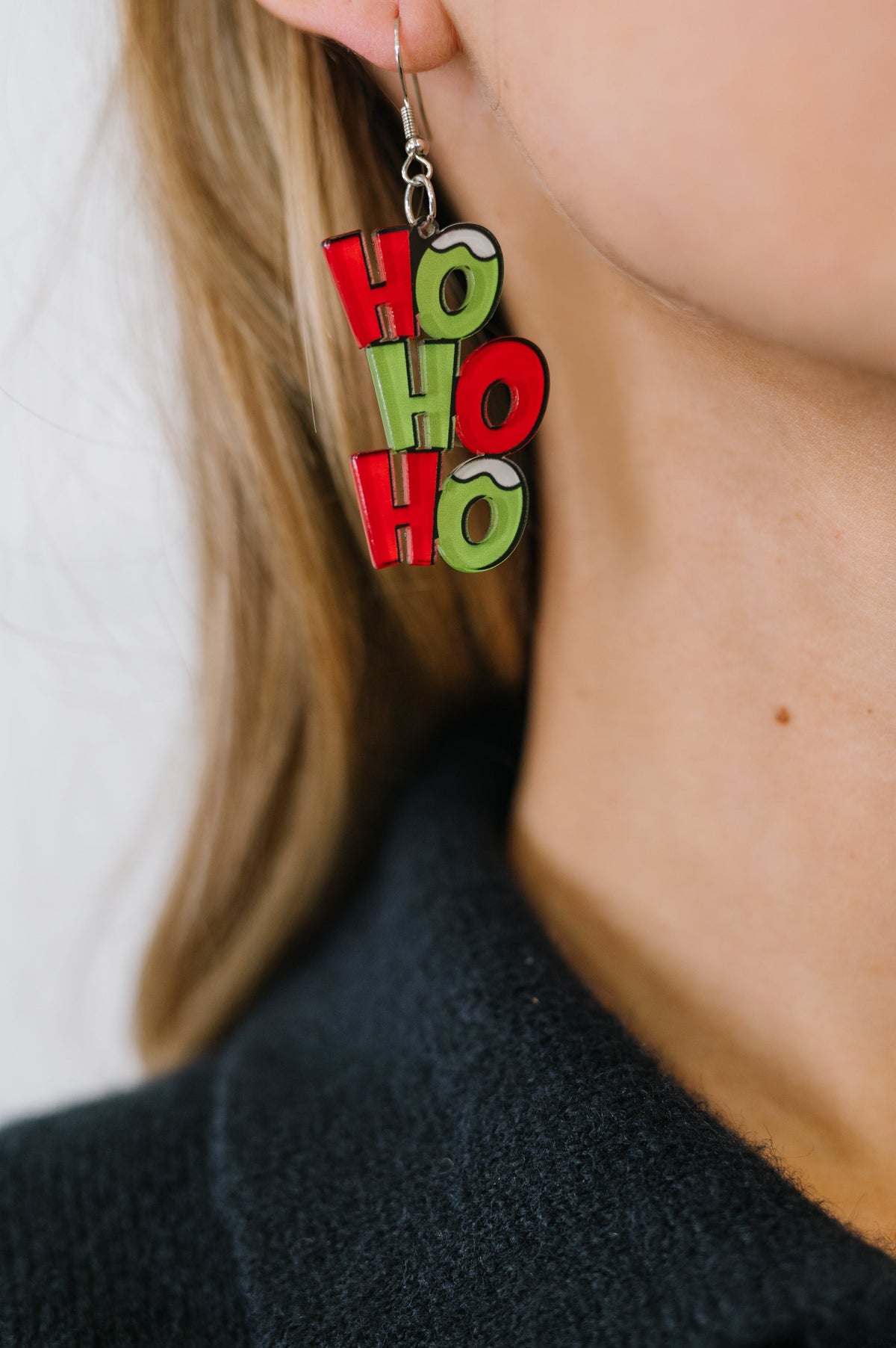 Earrings with 'HO HO HO' text worn by a person against a neutral background