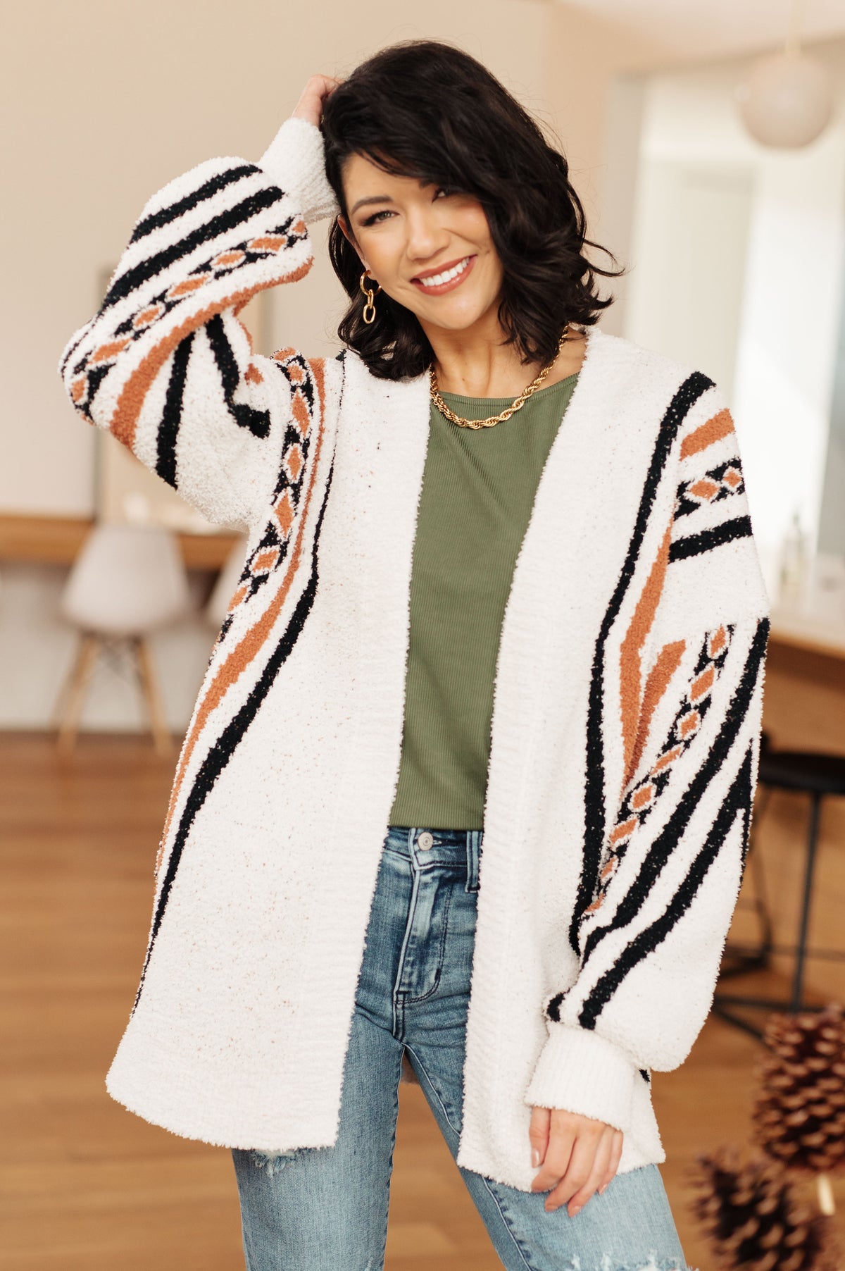 Woman wearing a white cardigan with black and orange patterns, standing indoors.