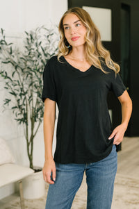 Woman wearing a black t-shirt and blue jeans standing indoors with a plant in the background